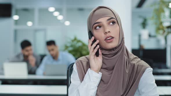 Serious Focused Arabic Female Millennial Manager in Hijab Talking on Phone Consulting Making