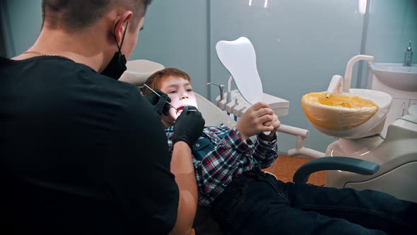A Little Boy Having a Treatment in the Dentistry - the Boy Holding a Mirror and Looking What's Doing