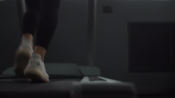 Closeup of Woman's Legs in Sneakers Walking on Treadmill at Gym Back View