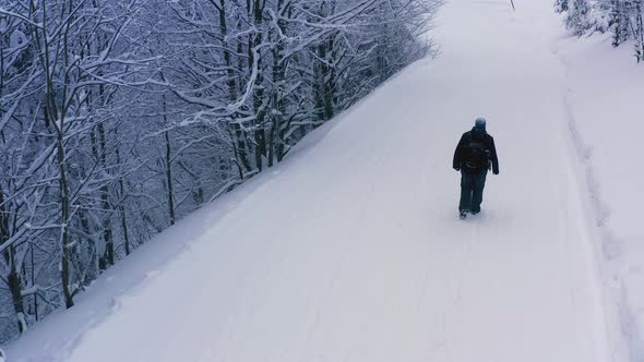 A Tired Tourist Walks Slowly in the Snow Along a Snowy Path in a Dense Forest