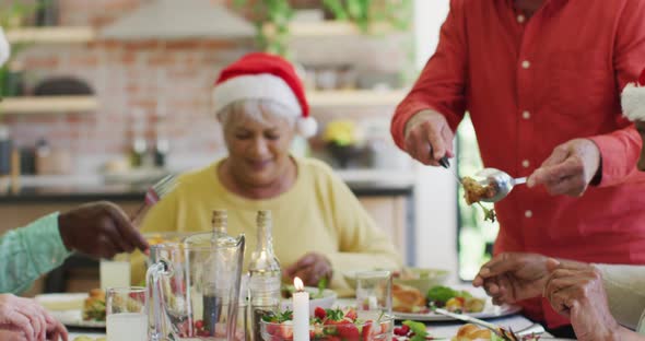 Caucasian senior man carving and serving turkey at christmas dinner table with diverse friends