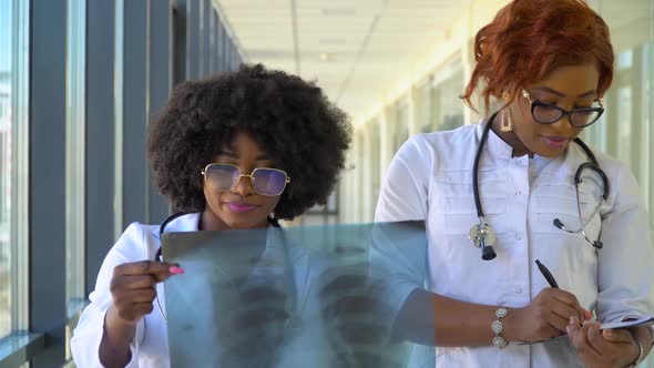 Two Female African-american Doctors Examines X-ray of Lungs, Holding It in Hands Indoors. Two