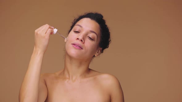 Beauty Portrait Young African American Woman Applying Skincare Serum on Face Rubbing Gently with