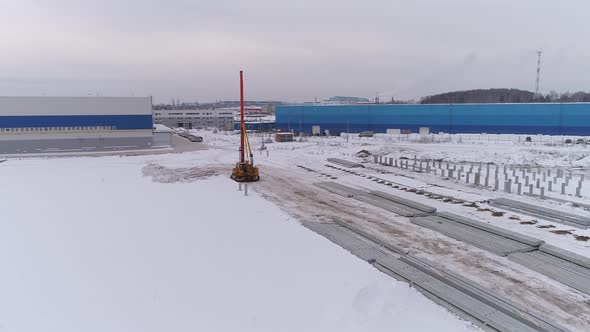 Aerial drone view of a lonely pile bore machine next to industrial buildings 05