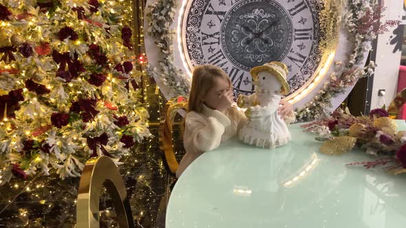 A Child Girl with a Snowman in Near a Christmas Tree with Big Clock