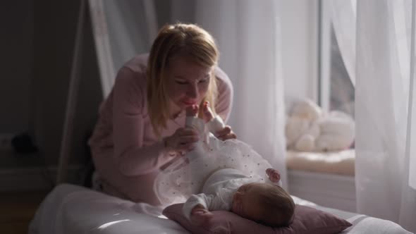 Newborn Baby Girl Lying in Sunny Living Room with Blurred Woman Kissing Little Feet