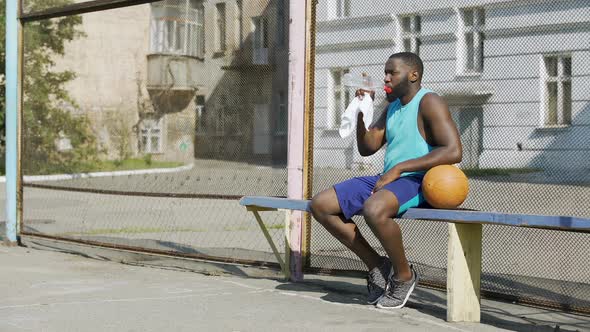 Strong Basketball Player Sitting on Bench and Drinking Mineral Water Sport