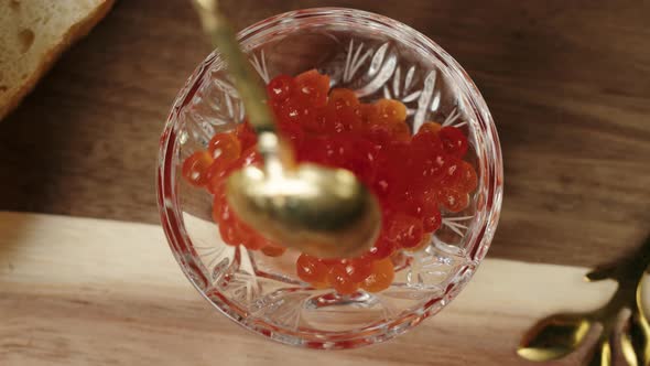 Putting Red Caviar with Spoon Into Glass Bowl Closeup