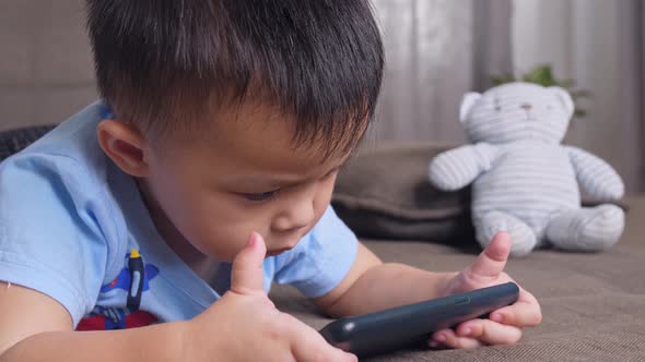 Asian Little Boy Laying On A Sofa Playing Smartphone