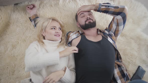Top View of Pretty Blond Caucasian Woman in White Sweater Lying with Boyfriend or Husband on Soft