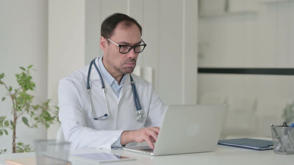 Middle Aged Doctor Working on Laptop in Office