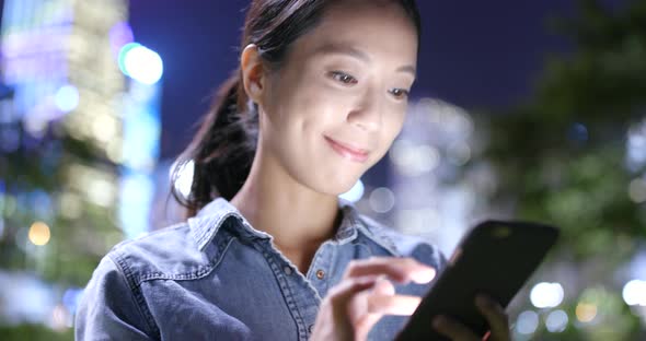 Woman sending text message on cellphone in the city at night 