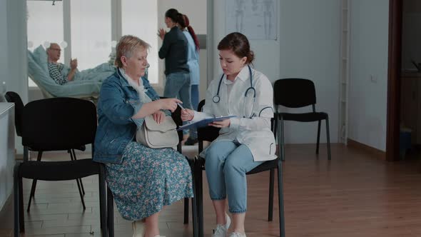 Aged Patient Signing Checkup Papers on Clipboard for Doctor