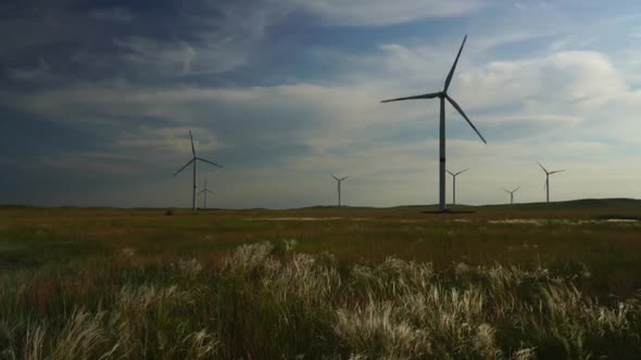 Motion the Blades of a Large Wind Turbine in a Field Against a Background of Cloudy Blue Sky with