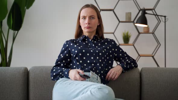 Closeup Portrait of a Young Woman Sitting on a Sofa Watching TV Holding a Remote Control Shocked By