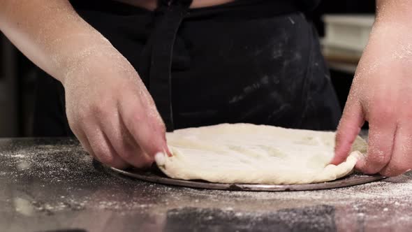 The pizzaiolo places the formed pizza dough on a tray. Cooking pizza in a pizzeria.