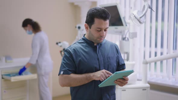 Thoughtful Professional Middle Eastern Doctor Typing on Tablet Entering Data As Caucasian Assistant