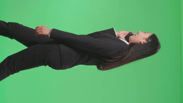 Side View Of A Smiling Asian Business Woman Talking On Mobile Phone While Walking On Green Screen