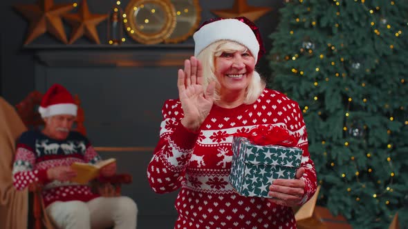 Senior Grandmother in Christmas Sweater Smiling Friendly at Camera and Waving Hands Gesturing Hello