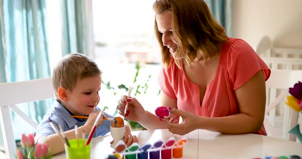 Young Mother and Her Son Having Fun While Painting Eggs for Easter