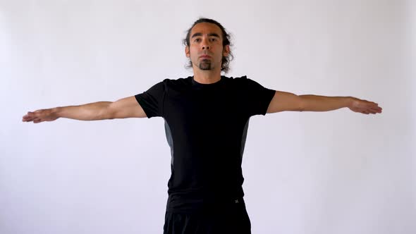 Hispanic Man with Long Hair and Goatee Doing Circular Shoulder Stretches Against White Studio Backdr