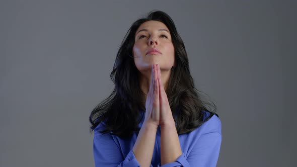 Adult Woman Praying Over Grey Background. Lady in Blue Shirt Begging Someone