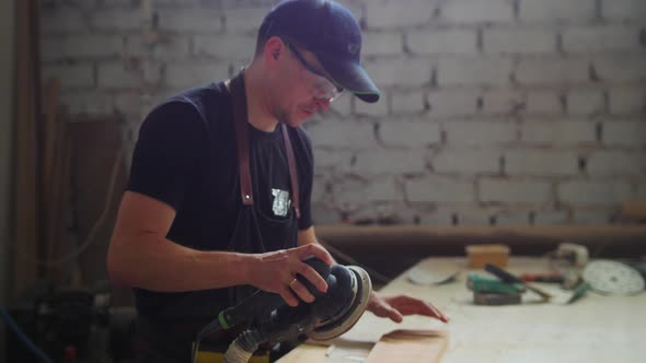 Carpentry Works  Man Worker in Protective Glasses Grinding the Surface of a Wooden Detail