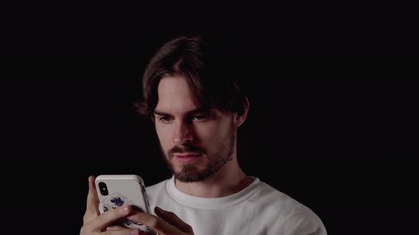Trendy Young Man using and considered typing on phone, close, black background