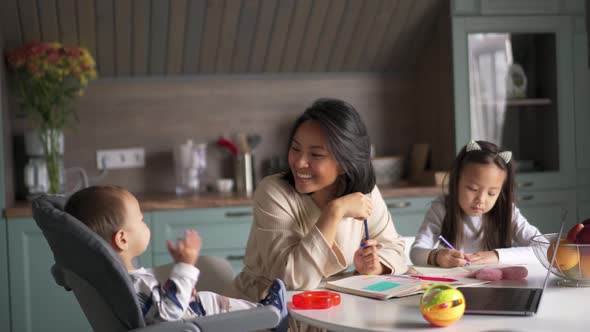 Happy Asian mother talking with her son while daughter painting in the kitchen