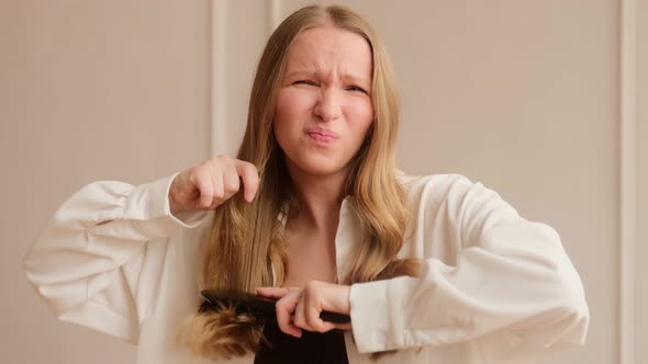 Young woman has problems with combing brushing her dry damaged hair with difficulty