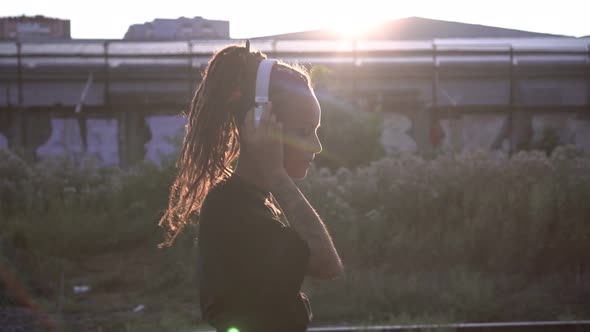 Modern Woman on the Background of the Sunset Listens to Music on Headphones