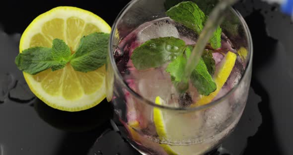 Pour Water in a Glass with Leaves of Mint, Lime, Lemon, Currants, Ice Cubes