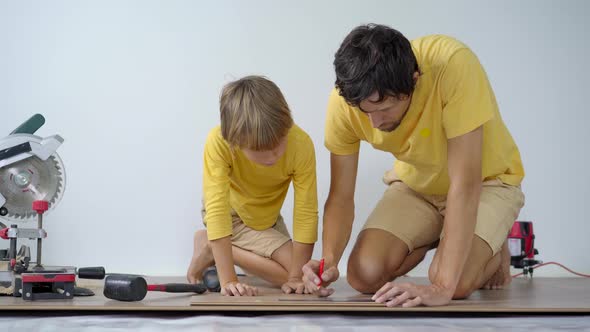 Father and His Little Son Install Laminate on the Floor in Their Apartment