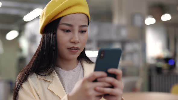 Asian Lady Typing Messages on Smartphone at Cafe