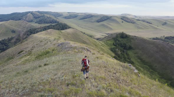 The Hiker with a Backpack Walking Along the Top of the Hill