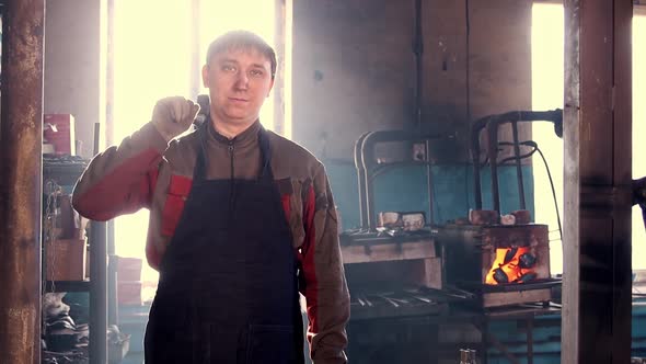 A Man Blacksmith Stands in the Workshop and Looking in the Camera