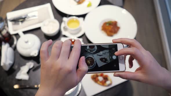 Woman Takes Pictures of Food on the Phone in a Cafe