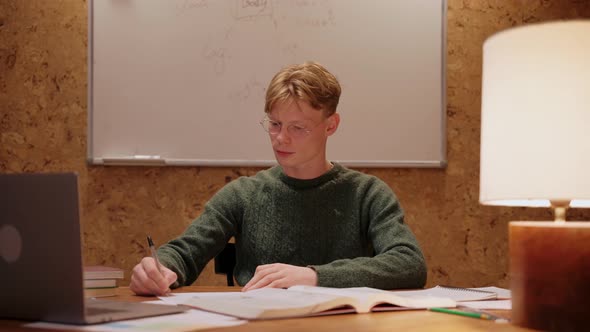 Guy Studying at Home Looks at the Laptop Writes a Notebook Looks at Camera