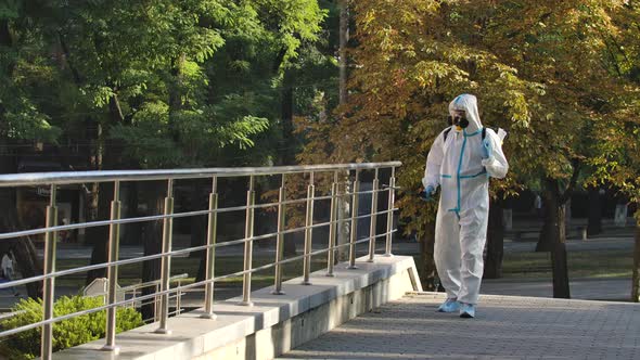 Man in a White Protective Suit Disinfects Handrails and Railings in a Public Area on a Deserted