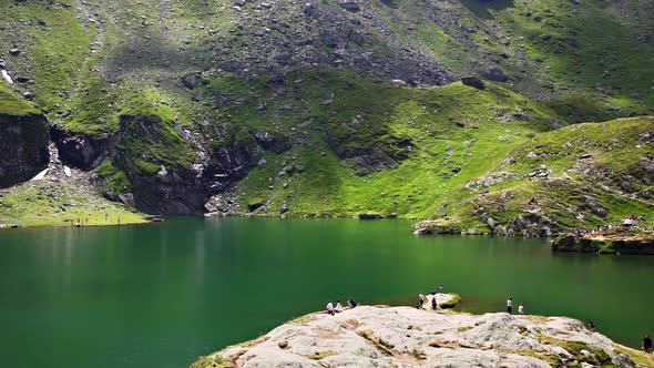 Aerial View Of Tourists Admiring Calm Green Waters Of Balea lake In the Fagaras Mountain, Romania. -