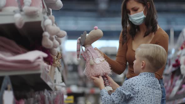 A Woman in a Mask with a Boy Choose Toys in a Super Market