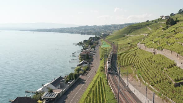 Aerial of train driving through beautiful Swiss landscape with hills and a large lake