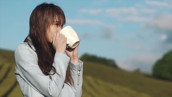 Charming Woman Is Drinking Tea From Big White Cup Standing on a Tea Plantation