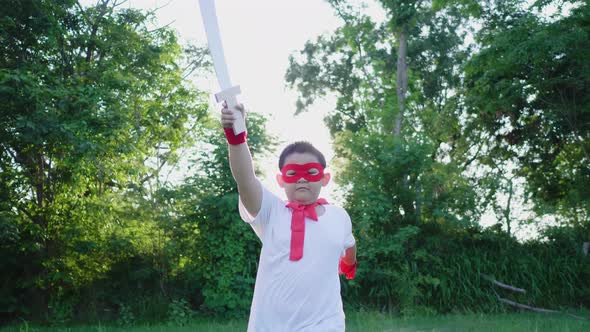 Front view of boy point sword up to the sky and walking come to camera in the park