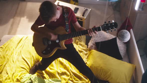 Teenager Playing Guitar on Bed