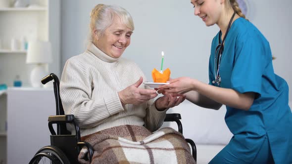 Doctor Giving Birthday Cake to Handicapped Woman, Aged Lady Blowing Out Candle