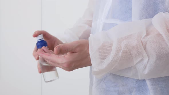 A Health Worker in a Washable Disposable Gown Disinfects the Skin of His Hands with a Sanitizer