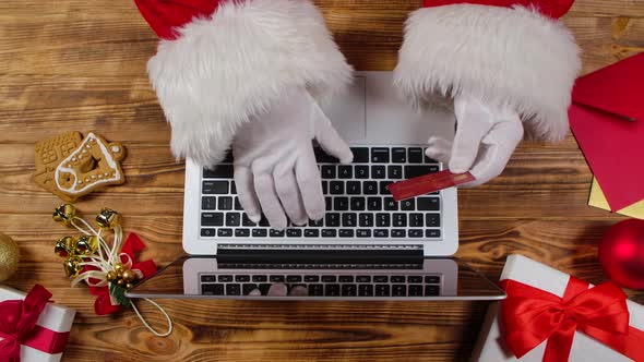 Top View Santa Hands in White Gloves are Typing on the Keyboard By Wooden New Year Decorated Table