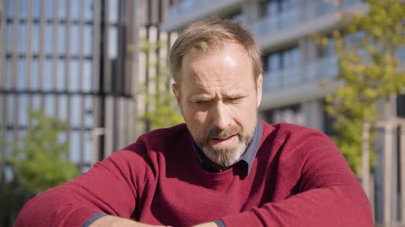 A Middleaged Handsome Caucasian Man Thinks About Something As He Sits in a Street