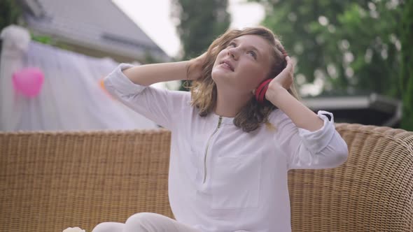 Portrait of Relaxed Teenage Girl Enjoying Music in Earphones Sitting on Backyard on Couch